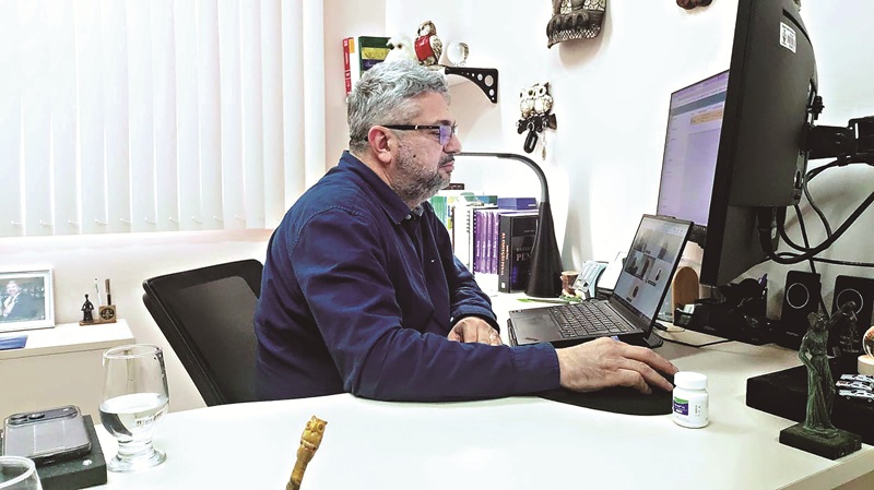 Homem de meia-idade com óculos usando laptop em um escritório, participando de uma videochamada.