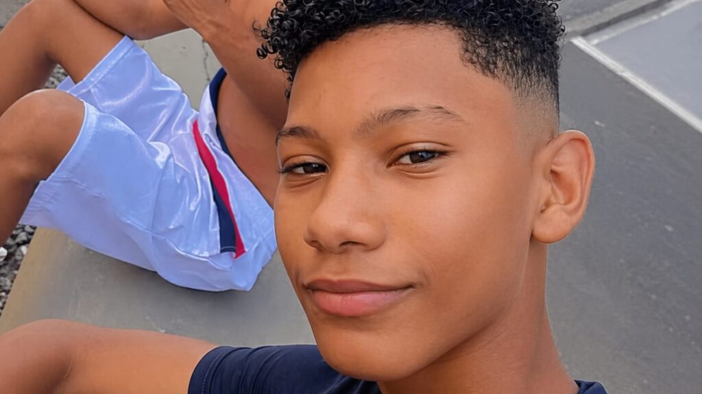 Close-up do rosto de um jovem negro com cabelo cacheado, olhando para a câmera.