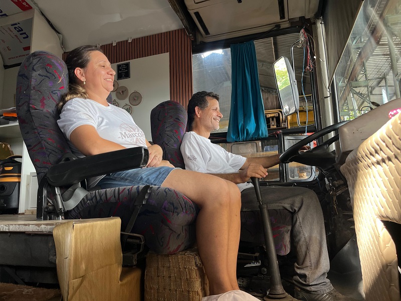 Casal sorrindo na cabine de um ônibus ou motorhome adaptado.