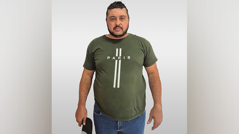 Homem de meia-idade com barba e camiseta verde 'PARIS' posando em fundo claro.
