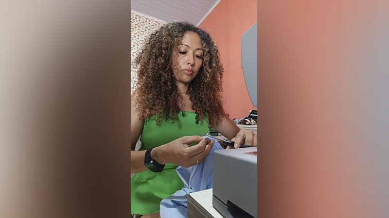Mulher com cabelo cacheado aparando tecido com tesoura perto de uma máquina de costura.