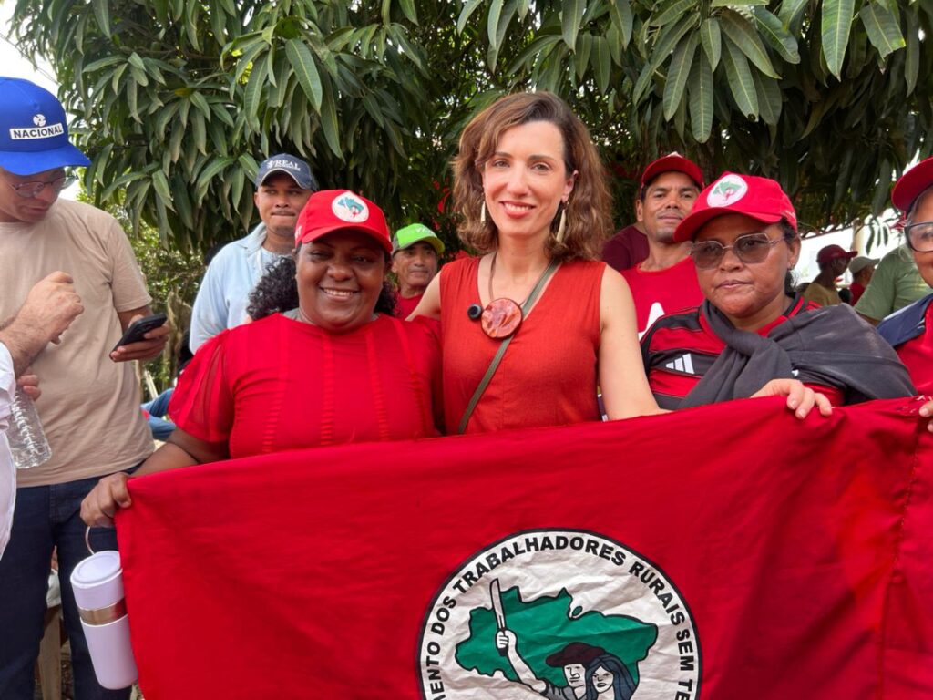 Grupo de pessoas sorrindo segurando a bandeira do Movimento dos Trabalhadores Rurais Sem Terra (MST).