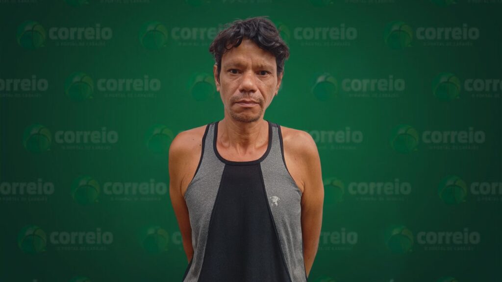 Homem de meia-idade com cabelo escuro e regata cinza e preta, olhando para a câmera em frente a um fundo verde com a palavra 'correio'.