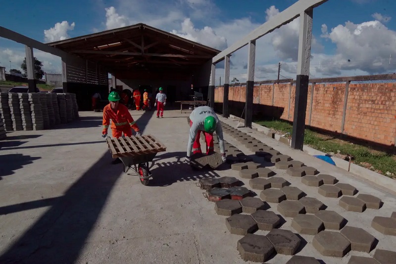 Trabalhadores com EPIs produzindo pavers hexagonais em fábrica ao ar livre.