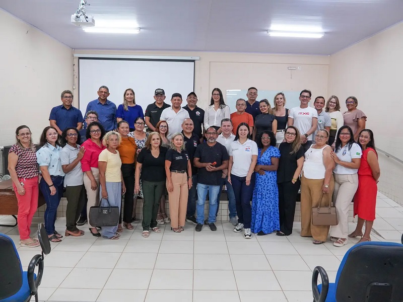 Grupo de pessoas diversas sorrindo em uma sala de reunião com um telão ao fundo.