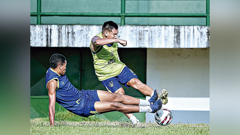 Dois jogadores de futebol em uma disputa intensa pela bola em campo de treino.