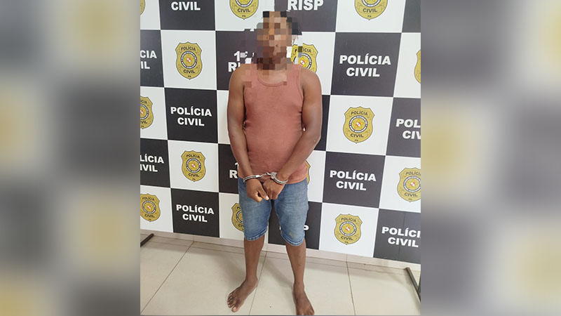 Homem algemado com rosto pixelado em frente a um painel da Polícia Civil.