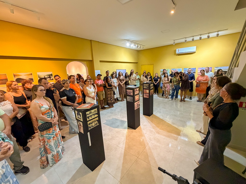 Grupo de pessoas em uma galeria de arte com fotos nas paredes e expositores centrais.