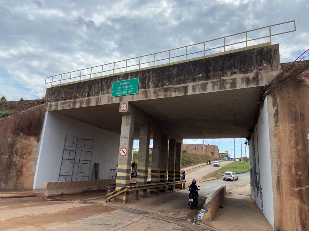 Viaduto ferroviário de concreto com estrada e veículos passando por baixo.