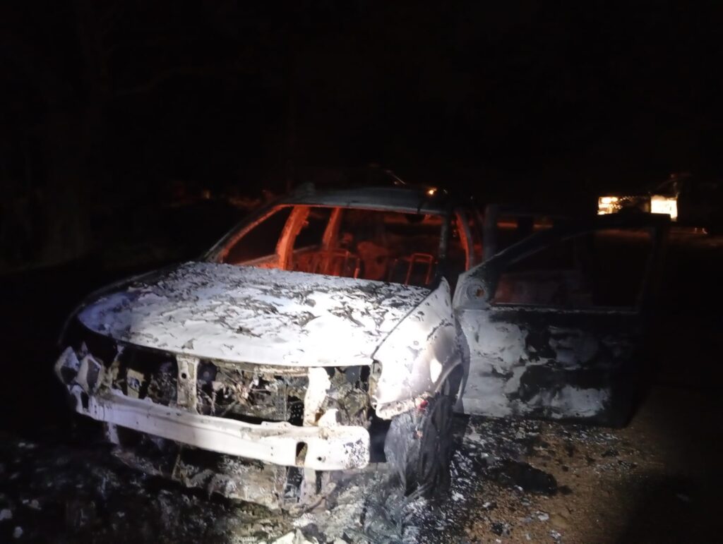 Carro queimado à noite, com o interior em brasa e exterior cinza de cinzas.