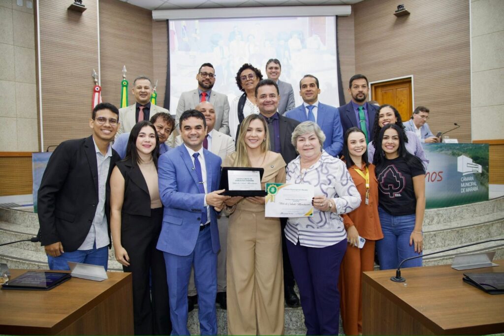 Grupo de pessoas sorrindo em evento formal, com três indivíduos recebendo prêmios no centro.