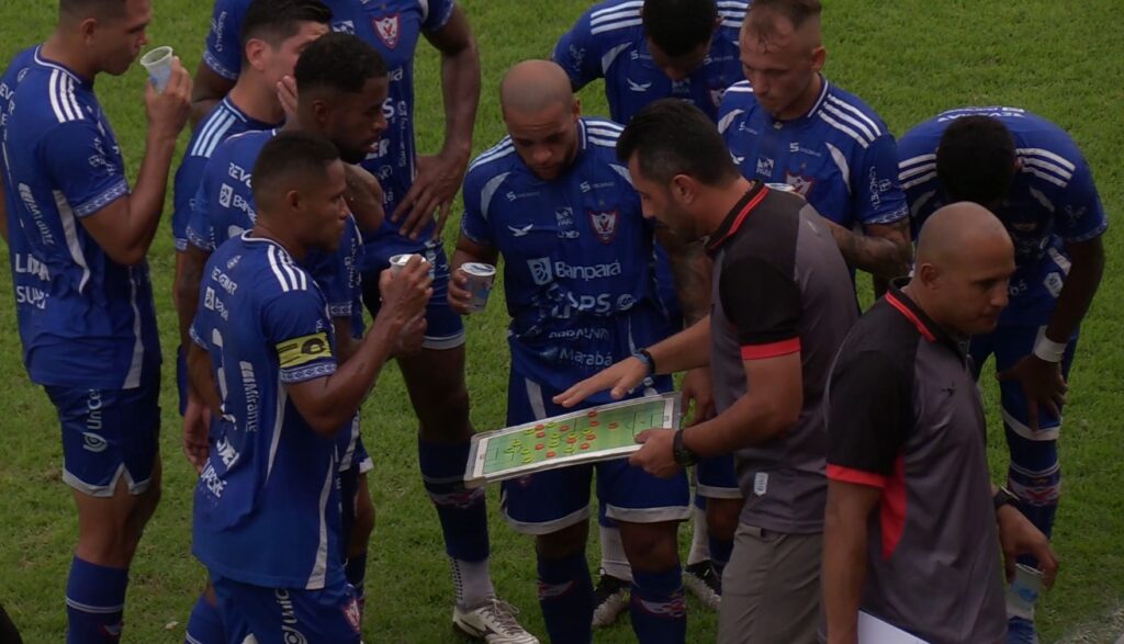 Treinador de futebol explicando tática a jogadores em campo.