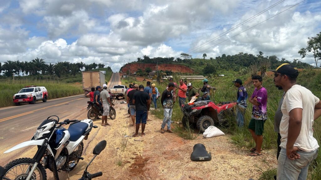 Grupo de pessoas na beira de uma estrada rural com um quadriciclo vermelho e motocicletas.