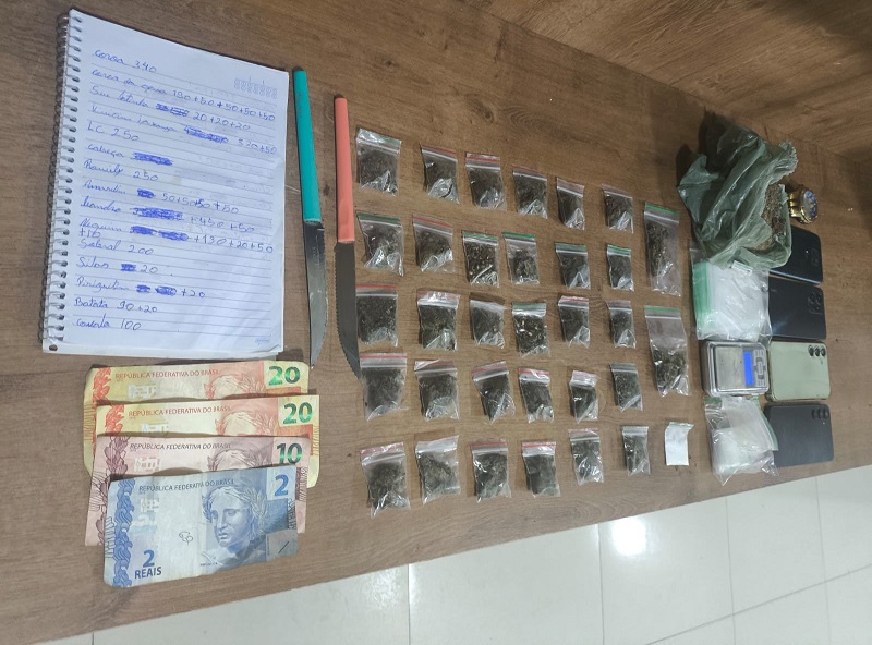 Itens apreendidos: drogas em porções, dinheiro, facas, celulares e balança em superfície de madeira.