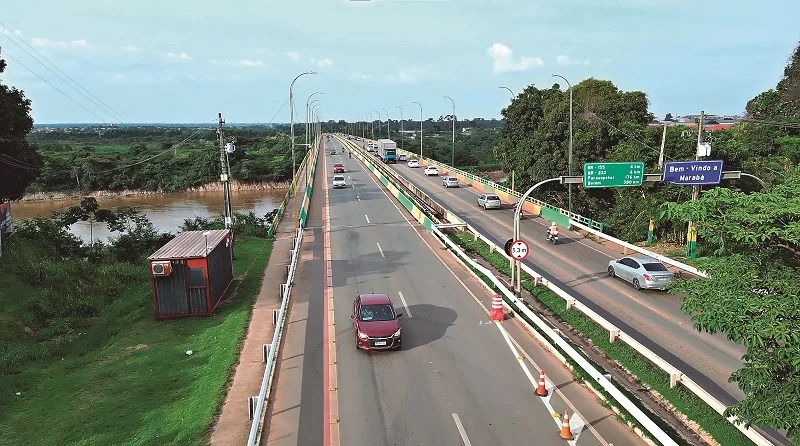 Ponte rodoviária movimentada sobre rio barrento, cercada por vegetação exuberante, com carros e sinalização de 'Bem-Vindo a Marabá'.