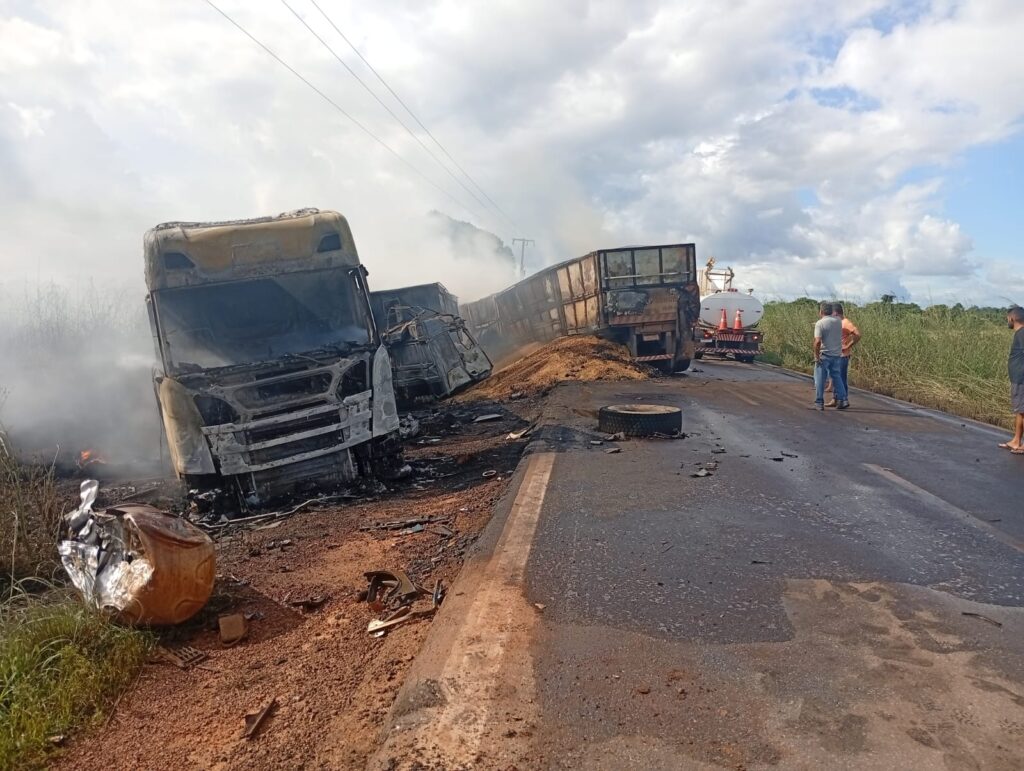 Acidente com dois caminhões em chamas na beira de uma estrada rural.