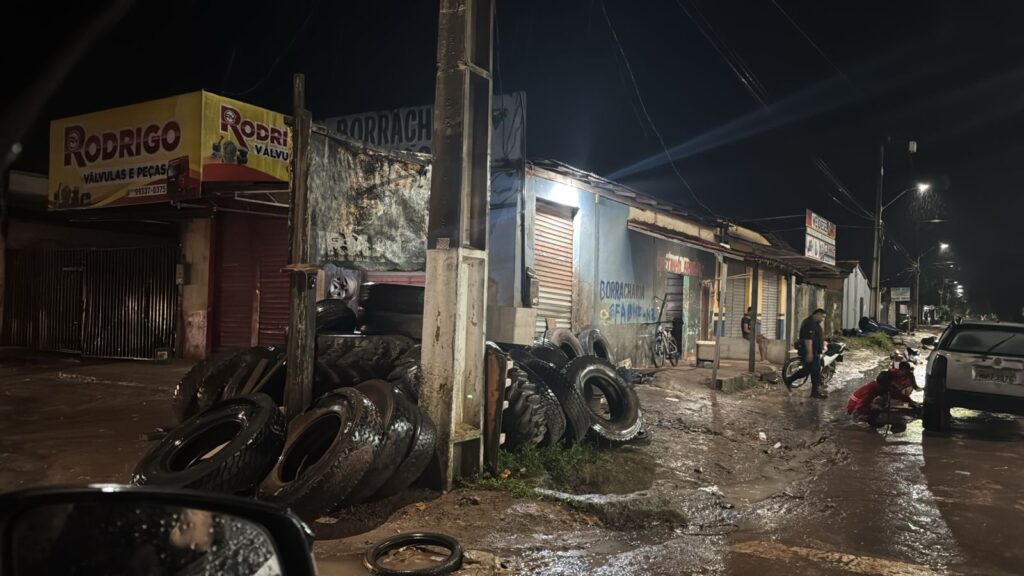 Borracharia à noite com pneus empilhados e rua molhada.