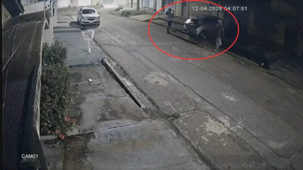 Câmera de segurança mostra dois homens ao lado de carro escuro em rua de madrugada.
