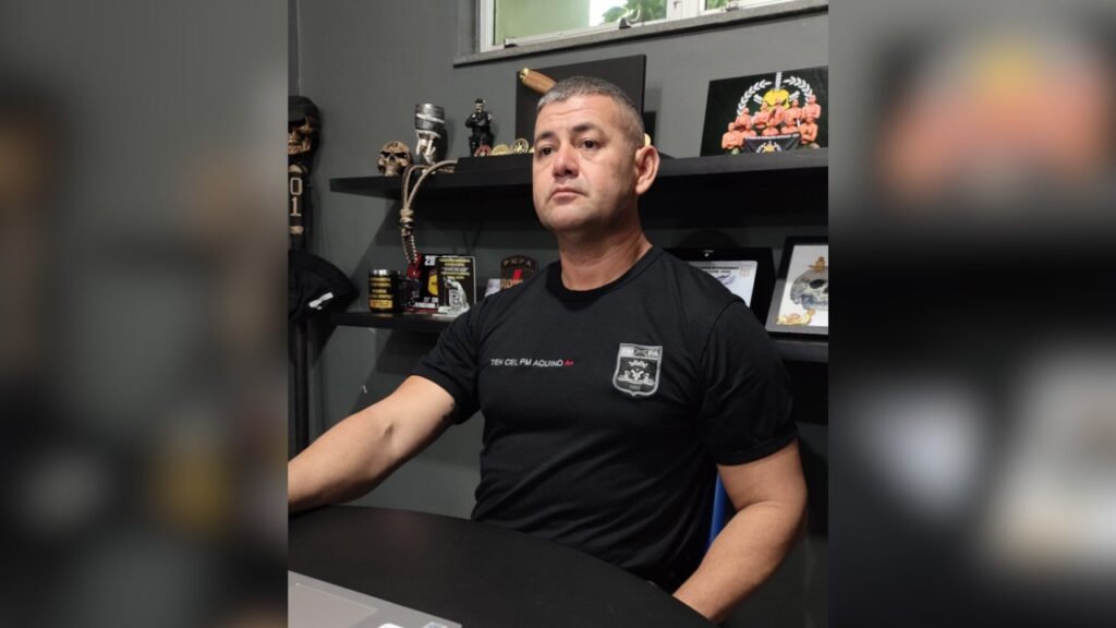 Homem de meia-idade com camiseta preta de oficial da PM em escritório.