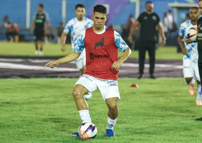 Jovem jogador de futebol driblando a bola em campo gramado.