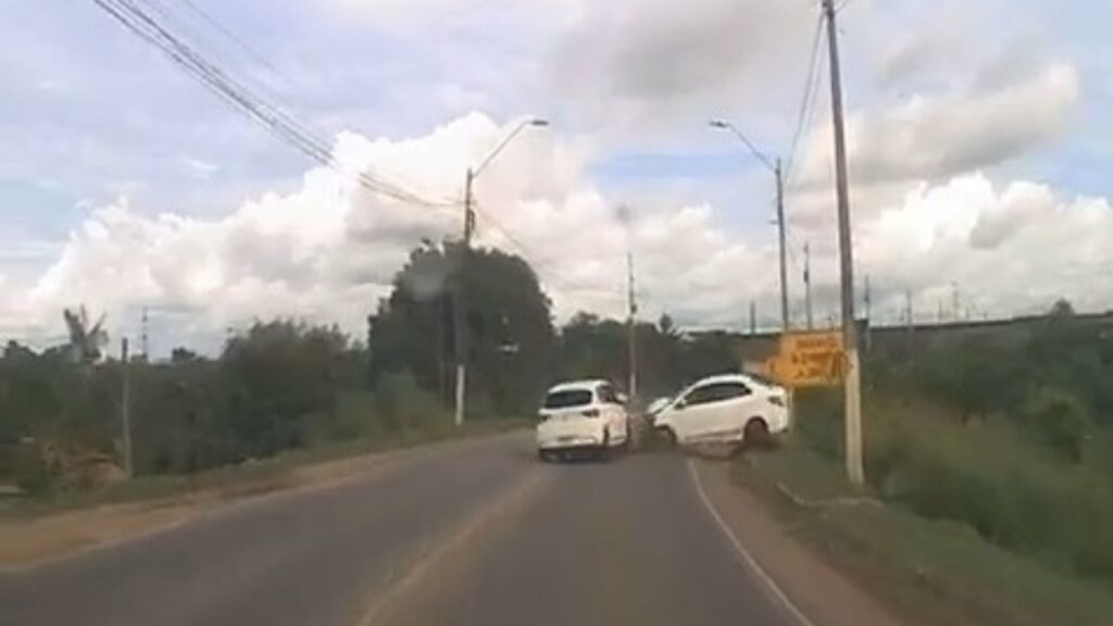 Dois carros brancos após um acidente em uma estrada rural com vegetação.