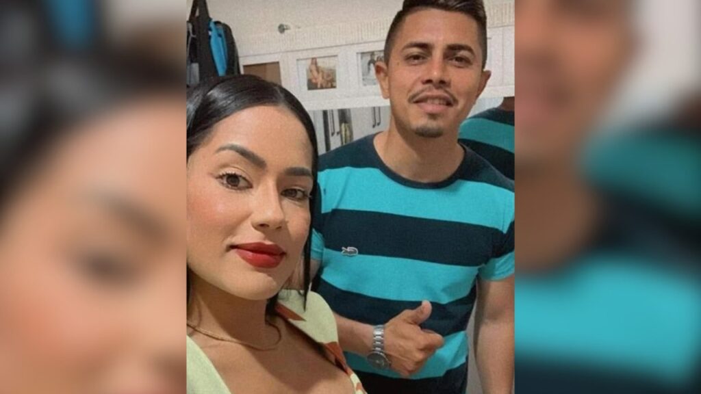 Casal sorrindo para selfie, ele com camiseta listrada e polegar para cima.