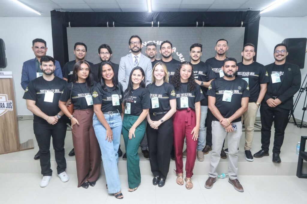 Grupo de pessoas em evento, a maioria com camisetas pretas "Sustentação Oral" e um homem de terno.