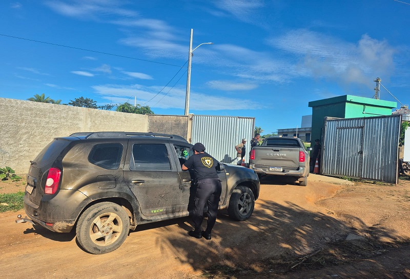 Um agente uniformizado inspecionando um SUV sujo em uma área de terra batida.