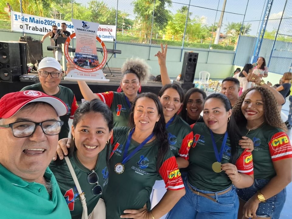 Grupo de pessoas, a maioria mulheres, sorrindo e celebrando com troféu e medalhas em evento do SINDECOMAR.