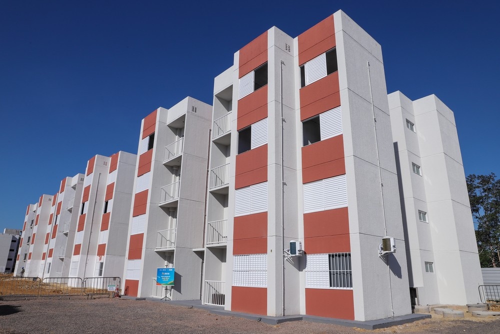 Prédios residenciais modernos com fachadas em cinza e terracota, sob céu azul claro.