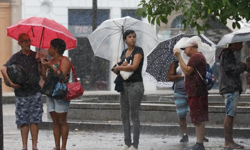 Pessoas com guarda-chuvas sob chuva forte em ambiente urbano.