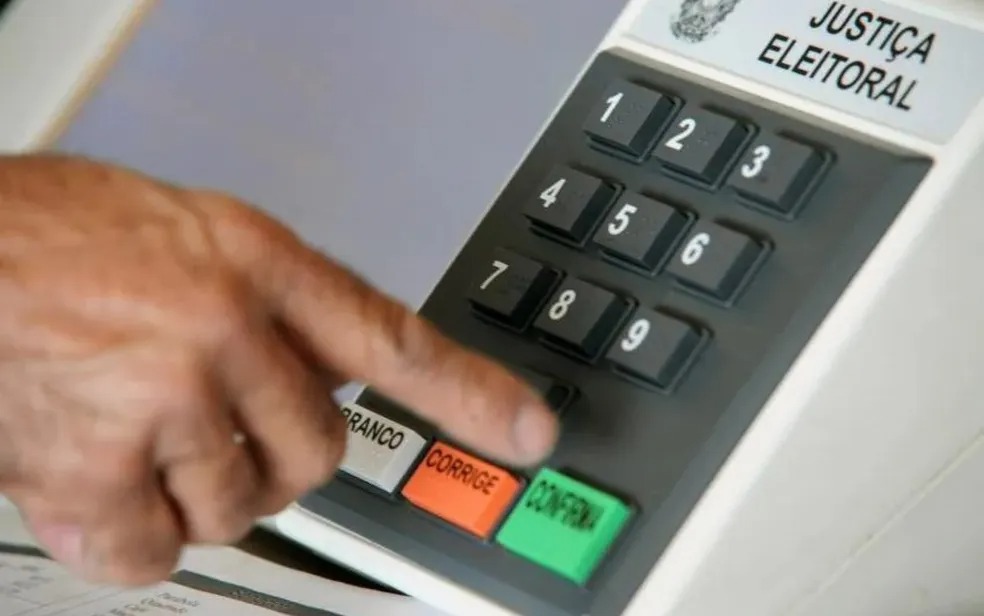 Dedo de eleitor pressionando a urna eletrônica em processo de votação.