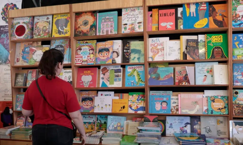 Mulher em frente a prateleiras cheias de livros infantis coloridos em uma livraria.