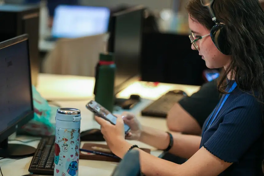 Pessoa usando celular e fones de ouvido em uma mesa de trabalho.