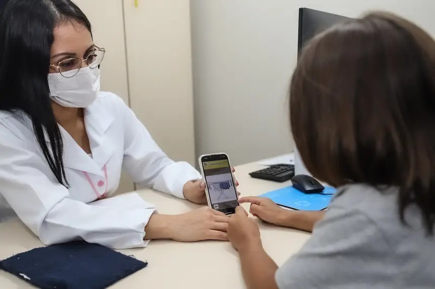Profissional de saúde com máscara mostra imagem em smartphone a paciente.