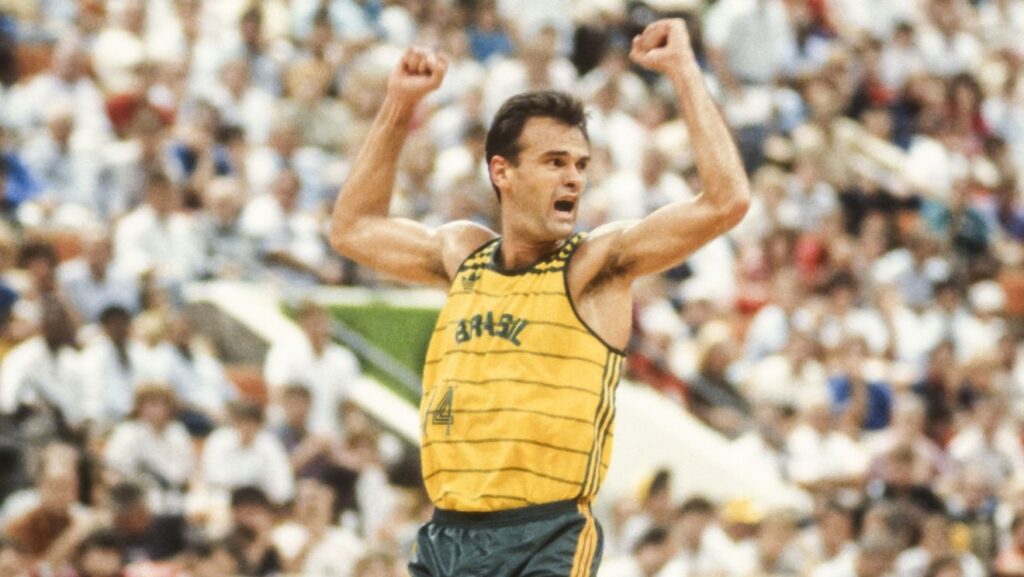 Jogador de basquete brasileiro em camisa amarela celebrando com punhos erguidos.