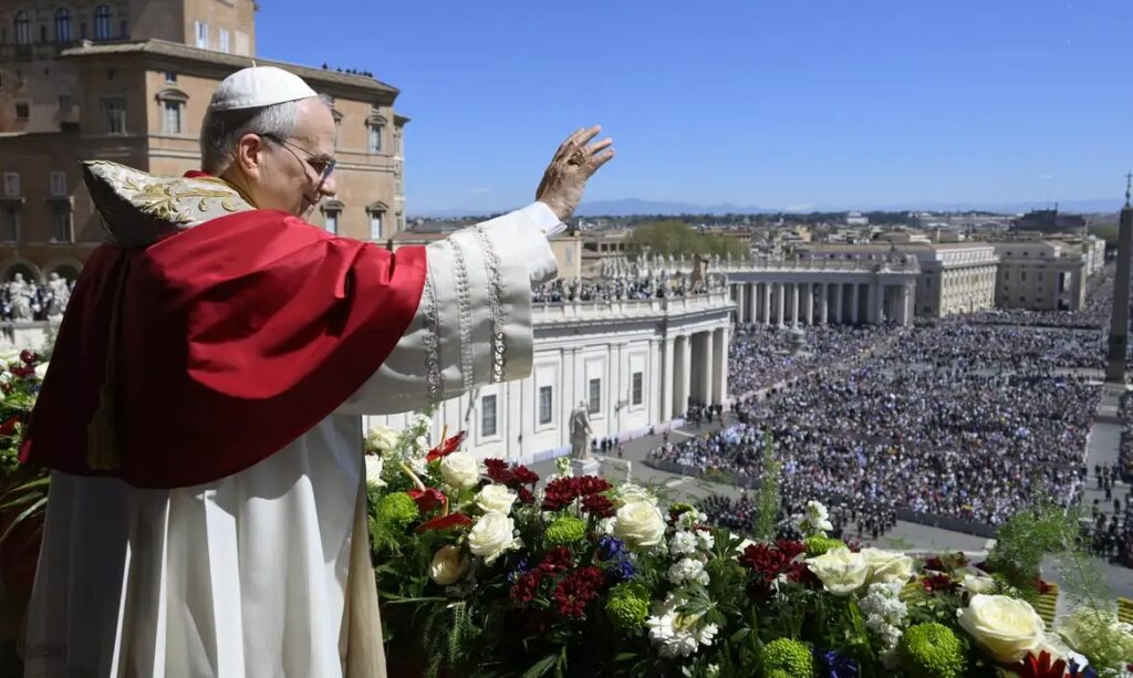 Papa Francisco acenando para a multidão na Praça de São Pedro de uma varanda florida.