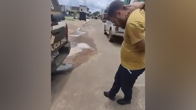 Homem de camiseta amarela sendo abordado próximo a uma viatura da Polícia Civil em rua.