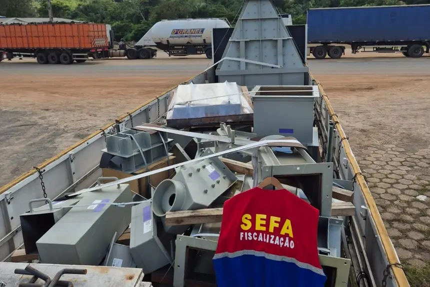 Jaqueta da SEFA Fiscalização em primeiro plano sobre peças de maquinário industrial em um caminhão.