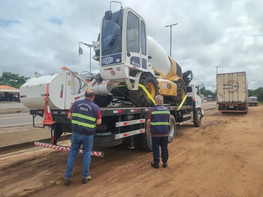 Homens da SEFA fiscalizando o transporte de uma betoneira autocarregável em um caminhão.