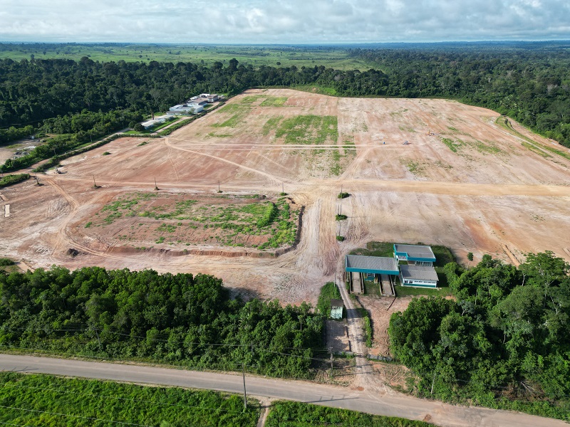 Vista aérea de uma grande área de terraplanagem cercada por floresta densa, com edificações e estradas de terra.