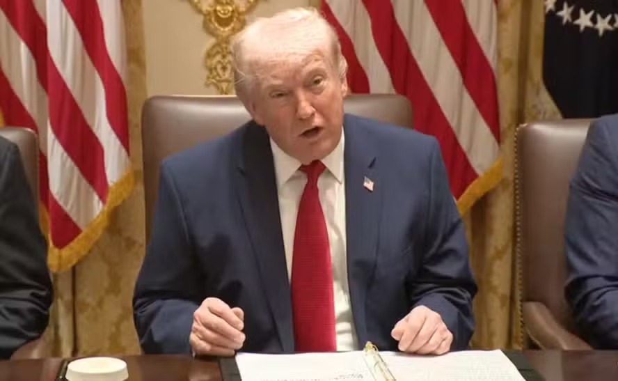 Donald Trump em reunião oficial com bandeiras dos EUA.