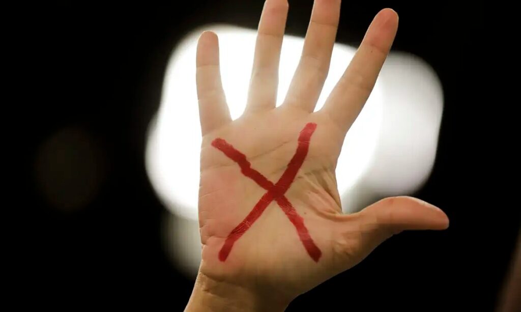 Mão aberta com um 'X' vermelho desenhado na palma.
