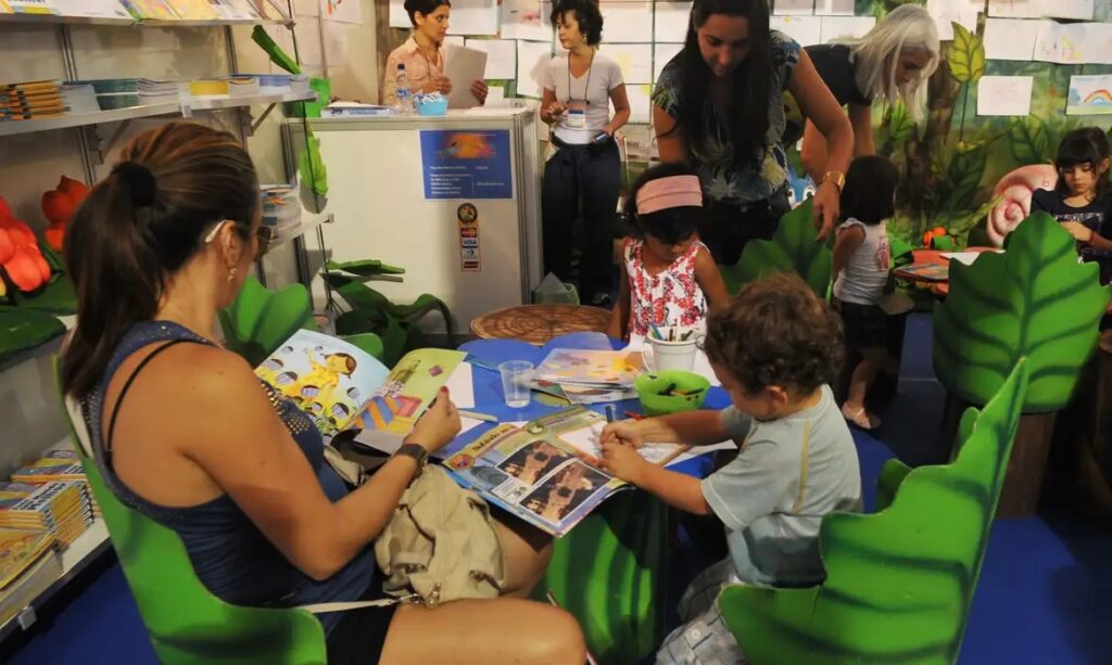 Crianças e adultos participando de atividades de leitura e desenho em um estande infantil.