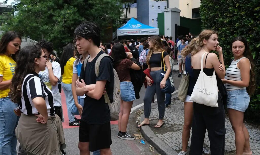 Jovem de mochila e braços cruzados entre grupo de estudantes em ambiente externo.