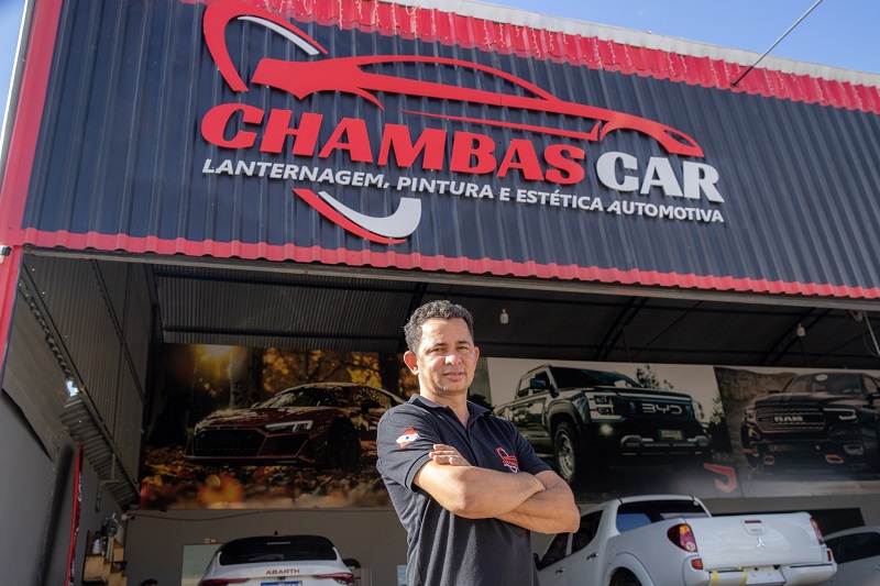 Homem em frente à oficina automotiva Chambas Car, que oferece lanternagem, pintura e estética.