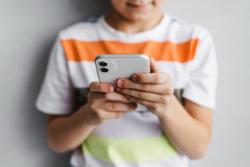 Menino segurando um smartphone com as duas mãos, focado na tela.