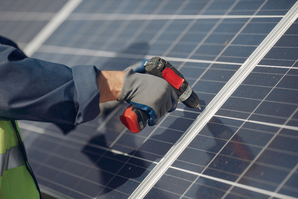 Mão com luva operando furadeira em painel solar.