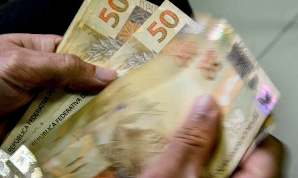 Mãos contando ou manuseando notas de R$50 reais.