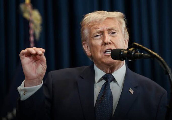 Donald Trump falando em um microfone com a mão esquerda levantada e gesticulando.
